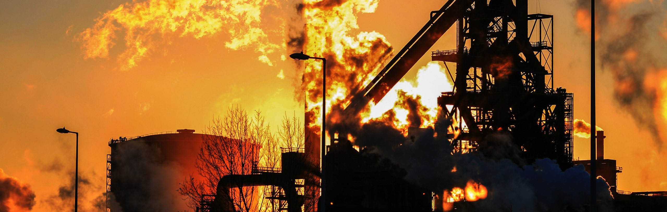 Steel mill industrial complex at dusk with flames and smoke