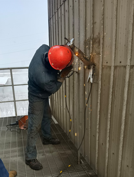 Technician welding a transducer mounting nozzle onto a large flue gas duct
